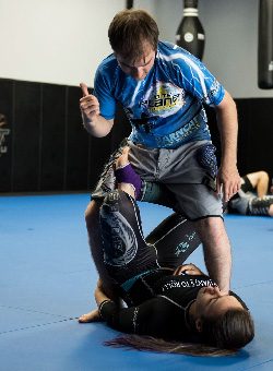 Full body shot of two 10th Planet Beaumont students practicing Brazilian jiu-jitsu X-guard, one male and one female.